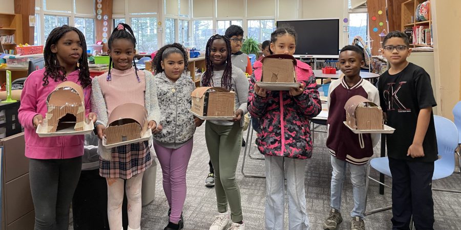 seven students holding their longhouses built out of cardboard