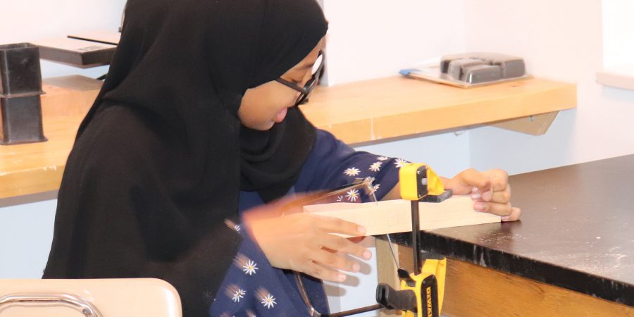Student in hajib cuts wood
