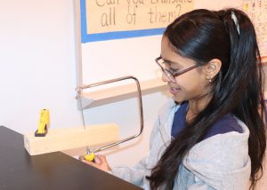 A girl cuts wood and smiles