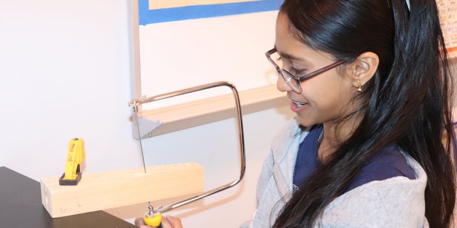 A girl cuts wood and smiles