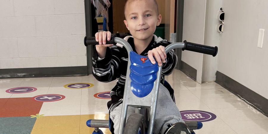 GageSmith_3rd_Grade A student rides a tricycle in the hallway