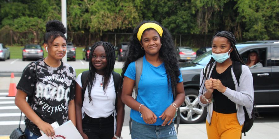 four students standing outside school with a parking lot behind them