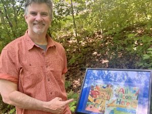 man stands near StoryWalk sign out in a wooded area