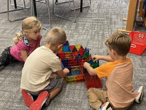 three students use magnetic pieces to build a house