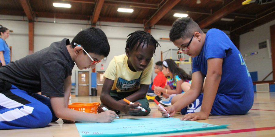 three students sitting on gym floor drawing