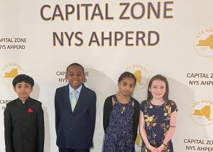 A group of four students in front of a banner recognizing their physical education achievement 