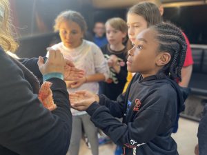 student holds out his hands for his turn as other students watch around him