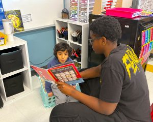 Student reading a book to another