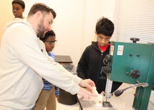 A teacher shows a student how to use a band saw 