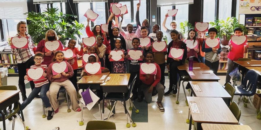 students standing together holding up white hearts of paper
